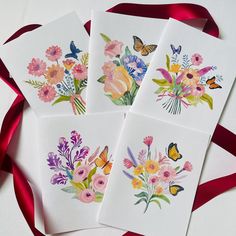 four cards with watercolor flowers and butterflies on them, tied to a red ribbon