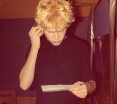 a young man holding a piece of paper while talking on a cell phone