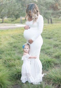 a pregnant woman and her child are standing in the grass