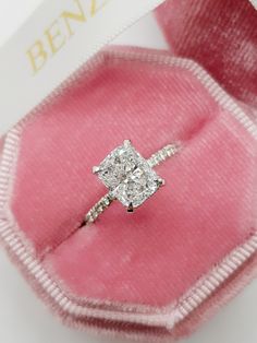 an engagement ring with a princess cut diamond set in a pink velvet box on top of it