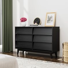 a black dresser in a white room with flowers and pictures on the wall behind it