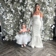 the mother and daughter are posing in front of a flower wall with white flowers on it