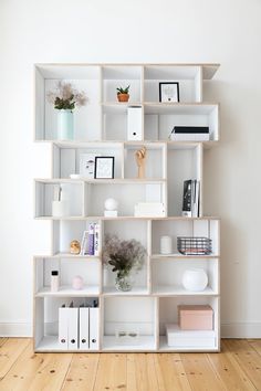 a white book shelf filled with books on top of a hard wood floor next to a wall