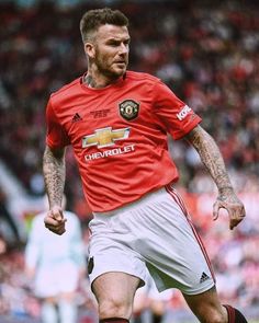 a man with tattoos on his arm kicking a soccer ball in front of a crowd