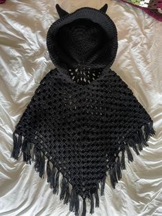 a crocheted black ponchle with a hood on it sitting on a white sheet