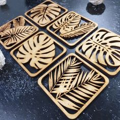 four wooden coasters with leaf designs on them sitting on a table next to rocks