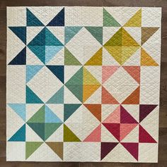 a colorful quilt on a wooden surface with many different colors and shapes in it,