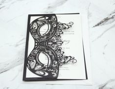 a black and white card with an intricate lace design on the front, sitting on a marble surface