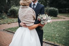 a man in a suit and tie holding a flower bouquet next to a woman in a white dress