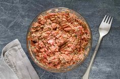 a glass bowl filled with meat next to a fork and napkin on top of a table