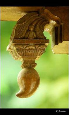 an ornate wooden object hanging from the side of a building with green trees in the background