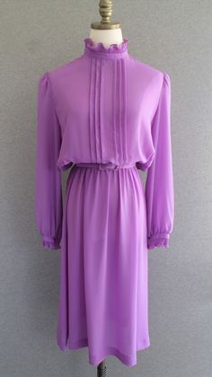 "This lilac dress features pin-tuck pleats down the front of the bodice to the elastic waist.   There are ruffles at the neck and cuff.   The belt is of the same fabric with the belt buckle being very slightly bent.  The belt is marked \"size 16\", but we thinks the size is more of a 10/12.  Check measurements. Estimated size 10/12 40\" bust 22-32\" waist 50\" total hip 44\" nape to hem  Purveyor's Note: We have searched far and wide, wrestled bears, braved the cold, traversed mountain ranges, f Elegant Purple Pleated Dress, Purple Pleated Wedding Dress, Formal Purple Dress With Pleated Bodice, Elegant Mauve Daywear Dress, Elegant Mauve Dress For Daywear, Party Dress Wedding, Lilac Lavender, Mountain Ranges, Dress Wedding Guest