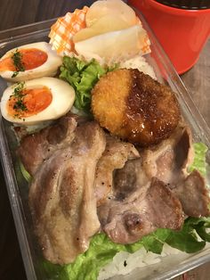 a plastic container filled with meat, eggs and lettuce on top of a wooden table