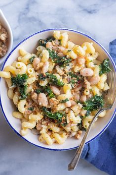 two bowls filled with pasta and spinach on top of a table next to a spoon