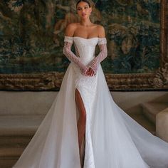 a woman in a white wedding dress standing next to a wall with a painting on it