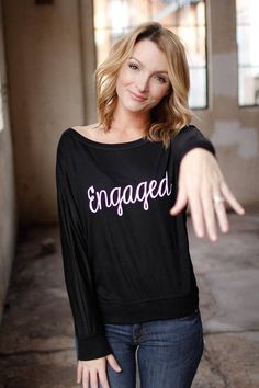 a woman pointing at the camera with her hand out and an engaged t - shirt on