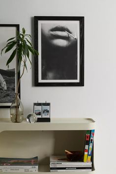 a white shelf with books and pictures on it next to a plant in a vase