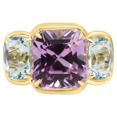 At the heart of this ring is a magnificent Kunzite Emerald Cut Center, boasting an impressive 11.45 carats. The soft purplish color of the Kunzite adds a touch of romance and femininity to the design, making it a standout feature. Flanking the Kunzite are two Aquamarines on each side, totaling to 4.16 carats. The serene blue tones of the Aquamarines beautifully complement the purplish hue of the Kunzite, creating a harmonious mixture of these two colors that is both eye-catching and enchanting. The bezel setting adds a modern and sleek touch to the ring, securing the gemstones in place allowing you to wear this ring without worry, while also allowing their beauty to shine through. Crafted from luxurious 14K Yellow Gold, the ring's warm and radiant tone further enhances the overall aestheti Luxury Kunzite Ring, Stone Fashion, Bezel Ring, Aqua Marine, Blue Tones, Exquisite Jewelry, Three Stone, Bezel Setting, Emerald Cut