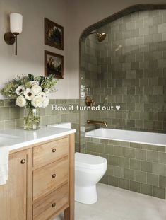 a bathroom with green tiled walls and white toilet next to a bathtub filled with flowers