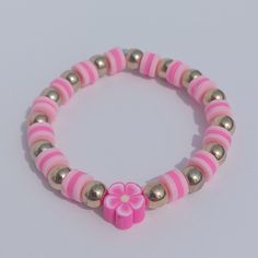 a pink and gold beaded bracelet with a flower on the clasp, sitting on a white surface