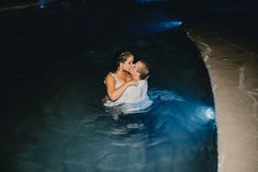 a man and woman are kissing in the water at night, while one holds his arm around the other's neck