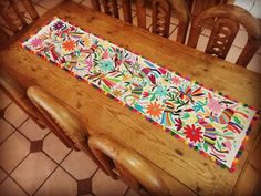 a wooden table topped with a multicolored floral runner on top of a tiled floor