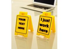 two yellow caution signs sitting on top of a white table next to a laptop computer