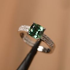 It is a green sapphire ring. The main stone is 7 mm*7 mm cushion cut.weight about 1.94 carats.The basic metal is sterling silver and plated with rhodium/14k white  gold/14k rose gold/14k yellow goldYou can also go to my shop Home for more elegant rings: https://www.etsy.com/shop/godjewelry?ref=hdr_shop_menu Customization is always welcome and please feel free to contact with me if you have any design ideas! Silver Emerald Ring With Cushion Cut, Green Cushion Cut Diamond Jewelry, Silver Emerald Square Cut Jewelry, Silver Emerald Jewelry With Square Cut, Silver Square Cut Emerald Jewelry, Silver Cushion Cut Ring With May Birthstone, Green Sapphire Jewelry With Halo Setting, Cushion Cut Gemstone Jewelry In 14k White Gold, Green Sterling Silver Square Cut Ring