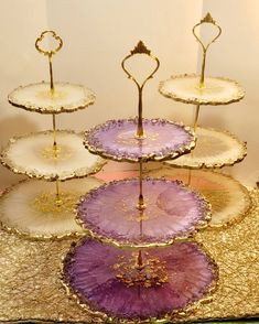 three tiered trays with purple and gold designs on them are sitting on a table