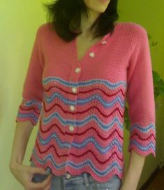 a woman standing in front of a green wall wearing a pink and blue striped sweater