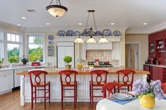 a large kitchen with red chairs and white counter tops in front of a center island