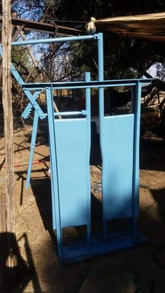 a blue trash can sitting on top of a dirt ground next to a wooden pole