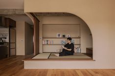 a woman sitting on top of a wooden floor in front of a book shelf filled with books