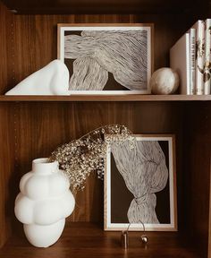 two white vases sitting on top of a wooden shelf next to pictures and books