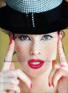 a woman with blue eyes wearing a black and white top hat, holding her hands up to her face