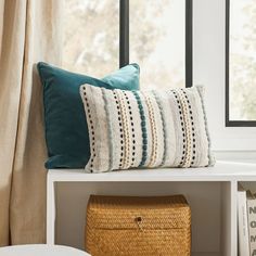 a white shelf with two pillows and a basket on top of it next to a window