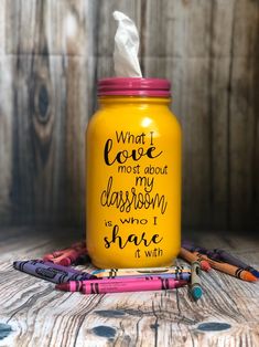 a yellow mason jar with writing on it and some crayons next to it