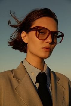 a woman in a suit and tie with her hair blowing in the wind while wearing glasses