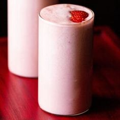 two glasses filled with milk and strawberries on a table