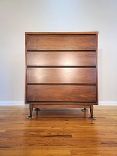 a wooden dresser sitting on top of a hard wood floor next to a white wall