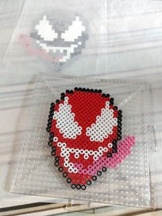 a red and white beaded brooch sitting on top of a plastic bag next to a sticker