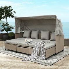 an outdoor daybed with a canopy over it on top of a wooden deck next to the ocean