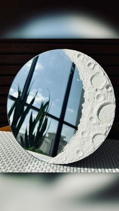 a white moon shaped mirror sitting on top of a table next to a potted plant