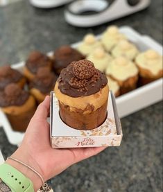 a person holding up a box of cupcakes in front of other desserts