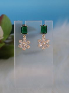 The Emerald Green CZ With Fancy Cut Clear Flower Fashion Earrings feature vibrant emerald green cubic zirconia at their heart, surrounded by intricately cut clear CZ petals in a captivating floral design. These stunning earrings blend the allure of precious gemstones with the finesse of floral motifs, offering a luxurious and eye-catching accessory for any special occasion. Length: 1.15 inches Width: 0.57 inches Closure: Butterfly Backs Material: Brass with 18K Gold Plating with Rhodium Coating Green Cubic Zirconia Crystal Earrings For Party, Green Cubic Zirconia Party Earrings, Green Cubic Zirconia Drop Earrings, Green Cubic Zirconia Earrings For May Birthstone, Elegant Green Flower Earrings For Gift, Green Flower Earrings For Wedding, Green Cubic Zirconia Flower-shaped Jewelry, Green Emerald Jewelry In Flower Shape, Green Flower Charm Drop Earrings