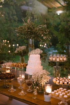 a table topped with lots of cakes and cupcakes next to candles in front of trees