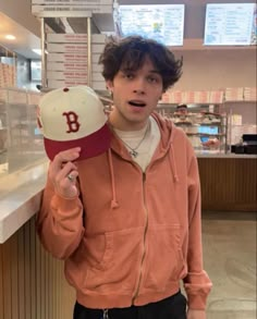 a young man holding up a baseball cap in front of a counter top display case