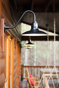 an outdoor light hanging from the side of a wooden building with chairs in the background