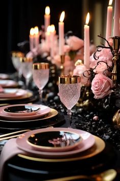 the table is set with black and gold plates, silverware, pink flowers and candles