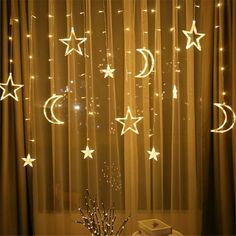 stars and moon string lights are hanging from the ceiling in front of a window with sheer curtains